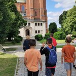 Alejką w kierunku bazyliki w Gnieźnie zmierzają dzieci. Na głowie mają założone słuchawki. Jeden z chłopców na plecach niesie plecak.