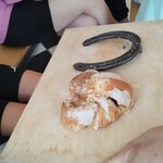 Na drewnianej tacy obok siebie leżą rogal marciński oblany lukrem oraz podkowa konia.