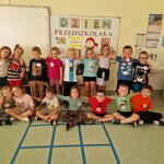 Dzieci z grupy sówki pozują do zdjęcia grupowego na tle napisu z okazji Dnia Przedszkolaka (1).jpg