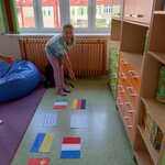 Na zdjęciu widnieje dziewczynka z kucykiem pochylająca się nad flagami różnych krajów, leżącymi na podłodze i wskazująca wyciągniętą ręką i palcem wskazującym na flagę Niemiec.