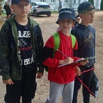 Trzech chłopców stoi_ jeden trzyma tabliczkę z kartą pracy_ w tle zabytkowy dworek.jpg