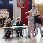 Trzy dziewczynki stoją wskazując na coś rękoma_ z tyłu dzieci w ławkach.JPG