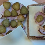 Na stoliku stoi talerz z kanapkami z chleba żytniego  z żółtym serem_ wędliną i kiszonym ogórkiem..jpeg