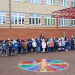 Grupa przedszkolaków z kokardami narodowymi stoi na patio_ w tle budynek szkoły z udekorowanymi świątecznie oknami.jpg