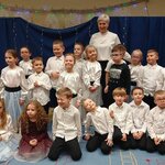 Grupa dzieci w białych bluzkach z osobą dorosłą w środku.jpg