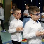 Trzech chłopców na pierwszym planie idzie niosąc lamipony. W tle -dziewczynki stoją ze świ.jpg