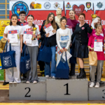 Grupa  stoi na podium z dyplomami i upominkami.png