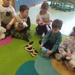 Dzieci z gr. Motylki siedzące na dywanie i zaglądające po kolei do ucha swojego pluszaka..jpg