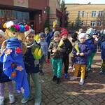 Dzieci stojace w parach przed szkołą z Marzanną i papierowymi_ wiosennymi kwiatkami..jpg