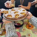  Na zdjęciu widać ręce trzymające talerz z ciastem. Wokół niego są inne ręce, które sięgają po kawałki ciasta.