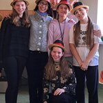 Na zdjęciu widać grupę osób - 5 dziewcząt i jedną kobietę. Wszystkie są uśmiechnięte, a na głowach mają czarno-czerwono-złote kapelusze. Jedna z dziewcząt kuca, a jedna ma uniesione do góry ręce.