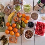 Na stole leżą różne produkty spożywcze - między innymi owoce, warzywa, chleby, pestki i orzechy.