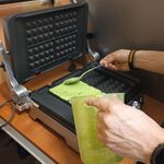 Widać rękę dorosłej osoby_ która nakłada łyżką zielone ciasto do gofrownicy.jpg
