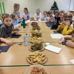 Dzieci siedzą wokół zsunietych w jeden stół ławek_ na których stoją talerze z 4 rodzajami gofrów.jpg