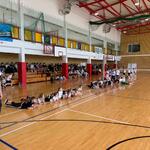 Grupa dzieci w strojach sportowych leży w rzędzie na brzuchach_ w lewej części widoczny wysoki mężczyna.jpg