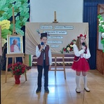 Duet_ dziewwczynka i chłopiec podczas wystąpu_ w tle tablice z logami patronów oraz napisem z nazwą konkursu.jpg
