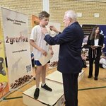 Chłopiec stojący na podium na II miejscu, otrzymujący medal od organizatora turnieju.