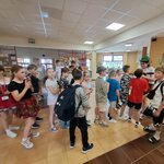  Na holu szkolnym stoi chłopak w zielonym kapeluszu, a przed nim mnóstwo dzieci.