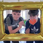  Na zdjęciu widać fotobudkę w formie złotego prostokątnego balona, a w niej  dwóch chłopaków trzymających symbole niemieckie - okulary w kształcie preclowych serduszek oraz rudą brodę.