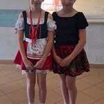 Na zdjęciu widać dwie dziewczynki. Jedna ma na sobie bluzkę i spódniczkę, a druga sukienkę w stylu bawarskim.