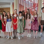 Na holu szkolnym stoi grupa dziewcząt i chłopców w tradycyjnych strojach bawarskich oraz strojach stylizowanych na bawarskie.