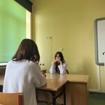 Dziewczyna  w fartuchu lekarskim przyjmuje pacjentkę przy biurku.jpeg