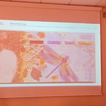 Prowadząca warsztaty kobieta omawia wyświetlony na ekranie nowoczesny banknot z ważką na pierwszym planie.jpg