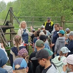 Uczestnicy wycieczki stoją przy drewnianych drabinkach_ które są przejściem do następnej zagrody.jpg
