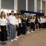 Uczniowie i nauczyciele ustawieni w kilku rzędach na sali gimnastycznej podczas uroczystego za-kończenia roku szkolnego 2024/2025. Większość osób ubrana jest odświętnie – w białe koszule i ciemne spodnie lub spódnice. W tle widoczna dekoracja z napisem „Uroczyste zakończenie roku szkolnego 2024/2025”, polska flaga i godło. Uczniowie są skupieni, wyglądają uroczyście.