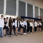 Grupa uczniów oraz rodziców stoi w rzędach na sali gimnastycznej podczas zakończenia roku szkol-nego 2024/2025. Uczniowie trzymają listy gratulacyjne, ubrani w odświętne stroje – białe koszule i czarne spódnice lub spodnie. W tle widoczna dekoracja z napisem „Uroczyste zakończenie roku szkolnego 2024/2025”, polska flaga oraz godło. Sala jest dobrze oświetlona, a uczniowie prezentują się radośnie i z zaangażowaniem.