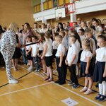Zdjecie przedstwia uczniów klas pierwszych w galowych strojach na sali gimnastycznej. Po l.jpg