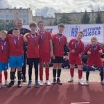 Grupa uczniów w czerwonych strojach sportowych stojących przed banerem programu Aktywnej Szkoły z trenerem. 