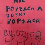 Czarny napis „Przemoc nie popłaca a dobro popłaca” na czerwonym tle. Pod napisem znajdują się narysowane trzy pieści uniesione w górę.