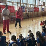 Mężczyzna trzyma młot_ obok stoi kobieta_ na podłodze naprzeciwko nich siedzą uczniowie.jpg