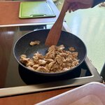 Na zdjęciu przedstawiona jest patelnia z kurczakiem i ręka ucznia, który miesza zawartość patelni.