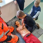 Uczeń uczy się wykonywać masaż serca na fantomie pod okiem ratownika_ drugi uczeń obserwuj.jpg
