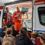 Ratownicy demonstrują spręt do pierwszej pomocy LUCAS_ uczniowe stoją przed karetką..jpg