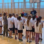 Dzieci w biało-czarnych strojach sportowych słuchają trenera.jpg