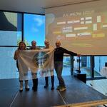 4 nauczycieli na scenie z banerem organizatora odbierających dyplom ukończenia na tle flag europejskich..jpg