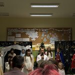  Na zdjęciu widać na pierwszym planie dwójkę dzieci: jedna dziewczynka – aniołek z aureolą oraz jeden chłopiec w białej koszuli w muszce, który właśnie mówi przez mikrofon. Za nimi stoi 5 dzieci, którzy patrzą się w przód oraz siedzi jedna dziewczynka skierowana do aparatu w białej bluzce. W tle widać dekorację zawieszoną na dwóch granatowych parawanach oraz dekorację zimową sali, którą widać na dwóch tablicach korkowych zawieszonych na ścianie. Z przodu zdjęcia widać głowy dwójki rodziców, którzy oglądają przedstawienie.