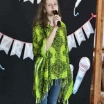 Uczestniczka konkursu ubrana na zielono z mikrofonem w dłoni.jpg