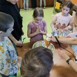Kilkoro dzieci stoi wokół stołu w sali kuchennej. Na blacie znajdują się miski_ a jedna z .jpg