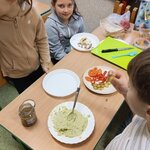 Przy stoliku stoją dzieci przygotowujące kanapki. Na talerzu leży zielona pasta_ a obok ro.jpg