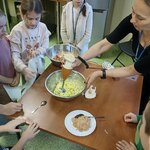 Osoba trzyma blender ręczny zanurzony w misce pełnej składników. Wokół stoją dzieci_ a na .jpg