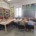 Na zdjęciu widać sześć dziewczynek pięciu chłopców, którzy siedzą przy stole. Troje z nich są odwróceni tyłem. Dzieci tworzą matryce do prac plastycznych. W tle widać dwa okna, obrazy powieszone za ścianach, tablicę korkową i półki wyposażone w materiały plastyczne.