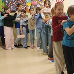 Na zdjęciu widać pociąg utworzony z 14 wesołych dzieci, który stoi na korytarzu. Pociąg ten trochę skręca i rusza do przodu. Jedna dziewczynka z pociągu trzyma torebkę ustami, przed nią widać dziewczynkę z różowymi zajęczymi uszami. Pociąg jest prowadzony przez chłopca w bluzce w paski. W tle widać dwie tablice korkowe, na których są umieszczone prace dzieci ze świetlicy.