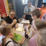 Dzieci stoją przy stoliku z książkami_ trzymają egzemplarze do podpisu. Osoba siedząca pod.jpg