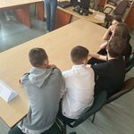 Przy stole siedzi grupa osób, a na stole leży kartka z napisem „REALNI”.