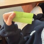 Osoba trzyma zieloną karteczkę z napisem „CYFROWI”, siedząc przy szkolnym stole.