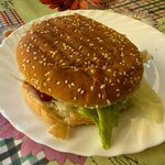 Na talerzu znajduje się gotowy burger w bułce z sezamem z sałatą i sosem.